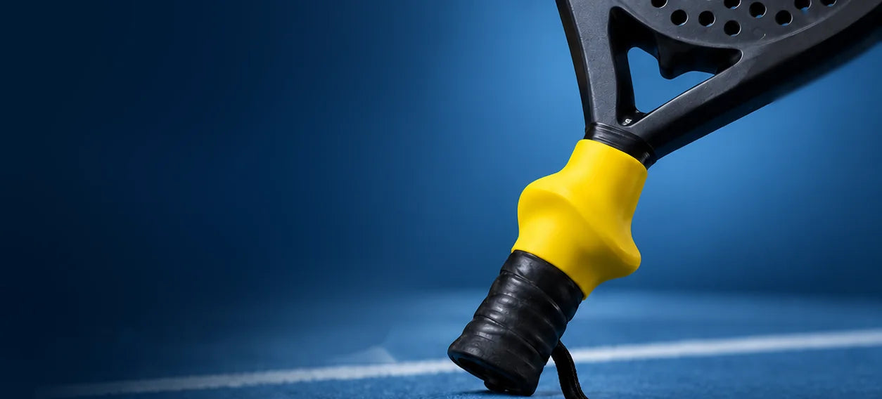 Ergo Grip jaune sur le manche d'une raquette de padel, sur un terrain bleu (mise en scène)