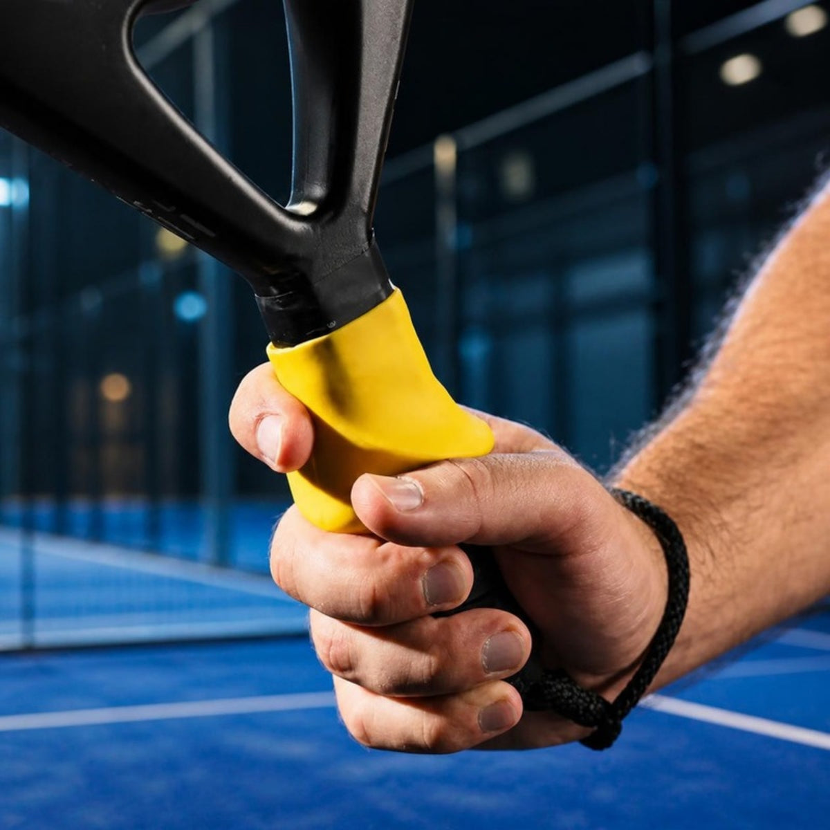 Prise en main : pouce et index posés sur l'Ergo Grip jaune, en haut du manche de la raquette de padel (photo fournisseur, décor modifié par IA)